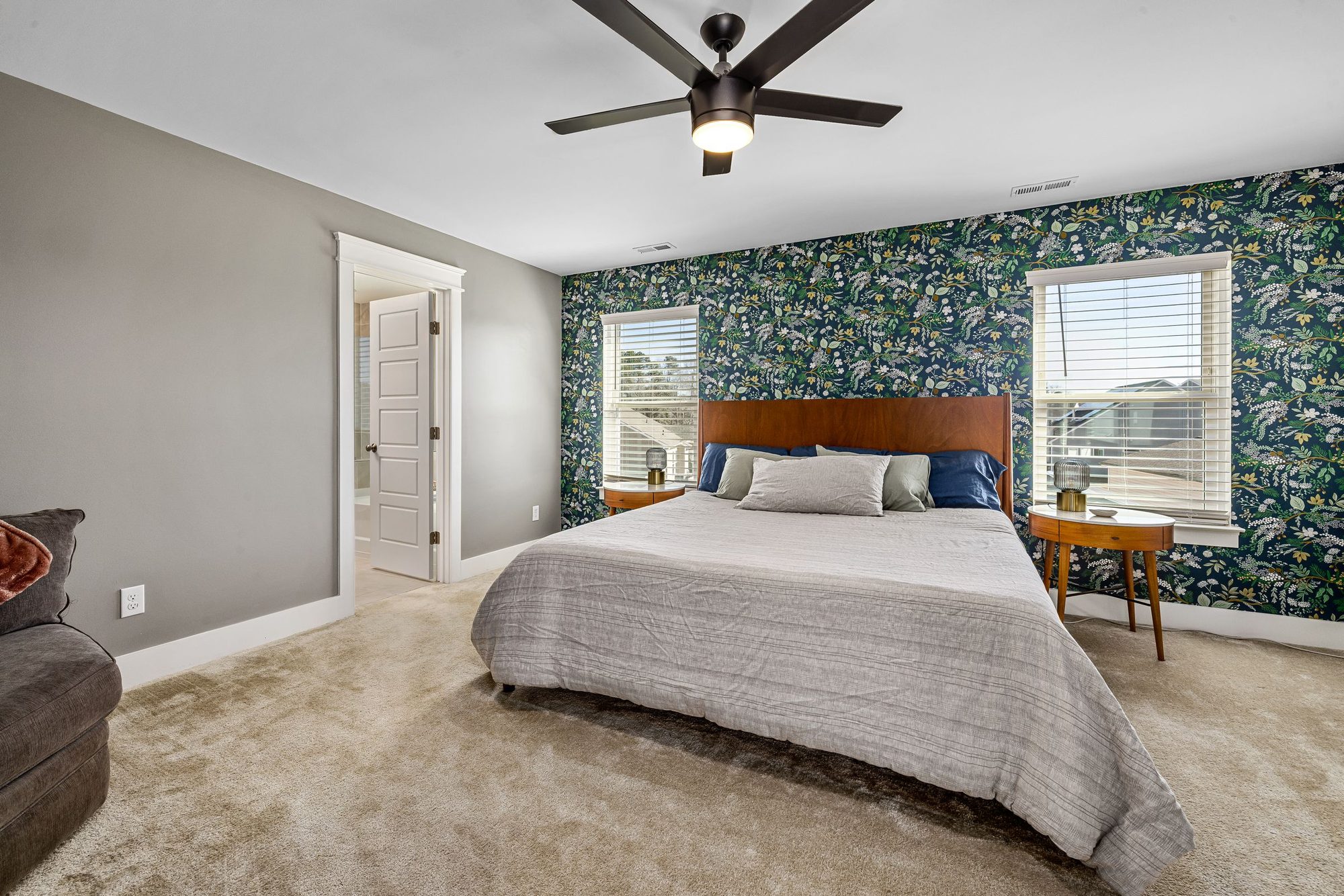 Bedroom with a dark botanical-print wallpaper accent wall behind a wood headboard, two windows and a ceiling fan