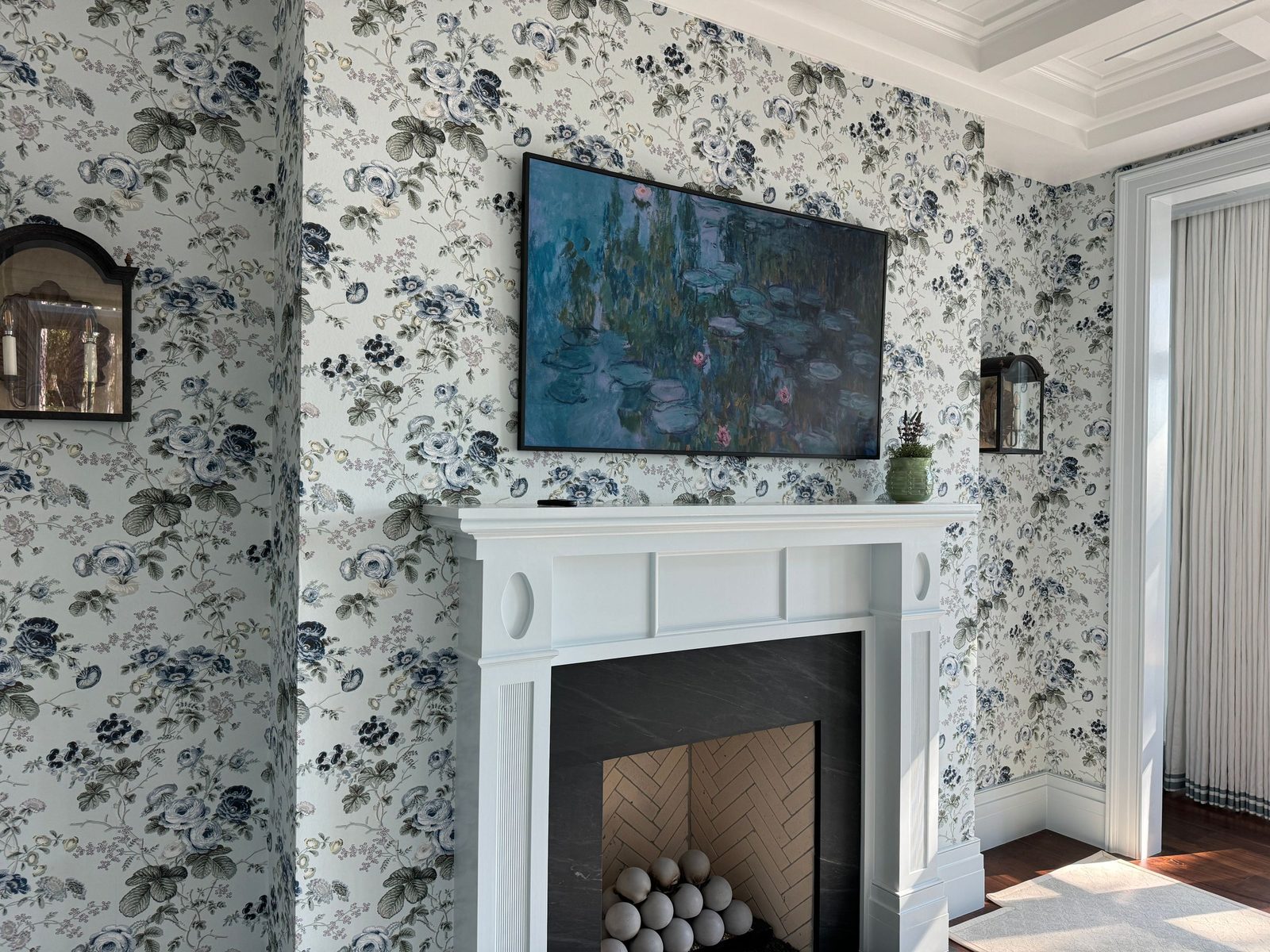 Living room with blue-and-white floral wallpaper surrounding a white fireplace mantel and a framed painting