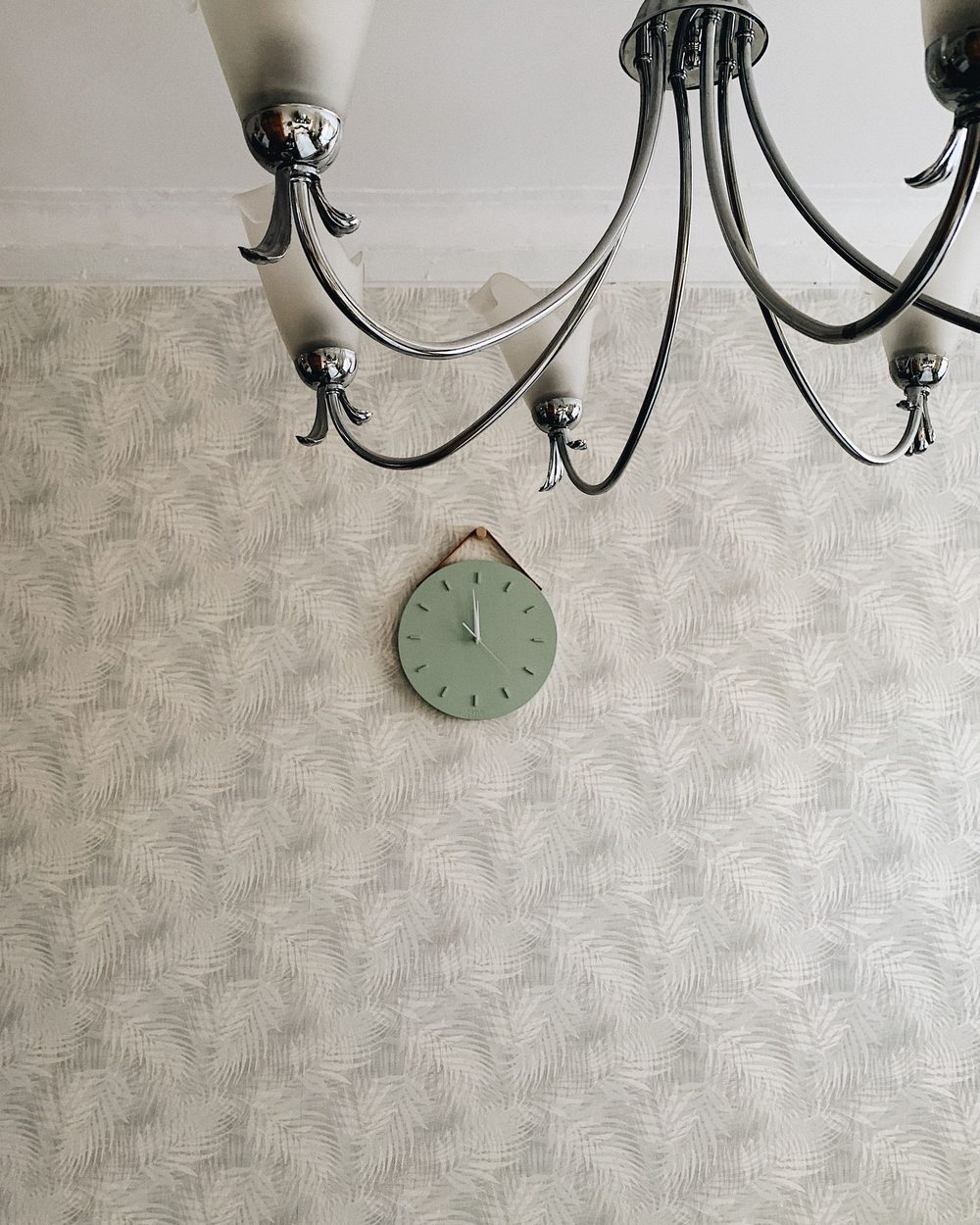 Wall detail with a subtle leaf-patterned wallpaper, a small sage wall clock and a black chandelier arm